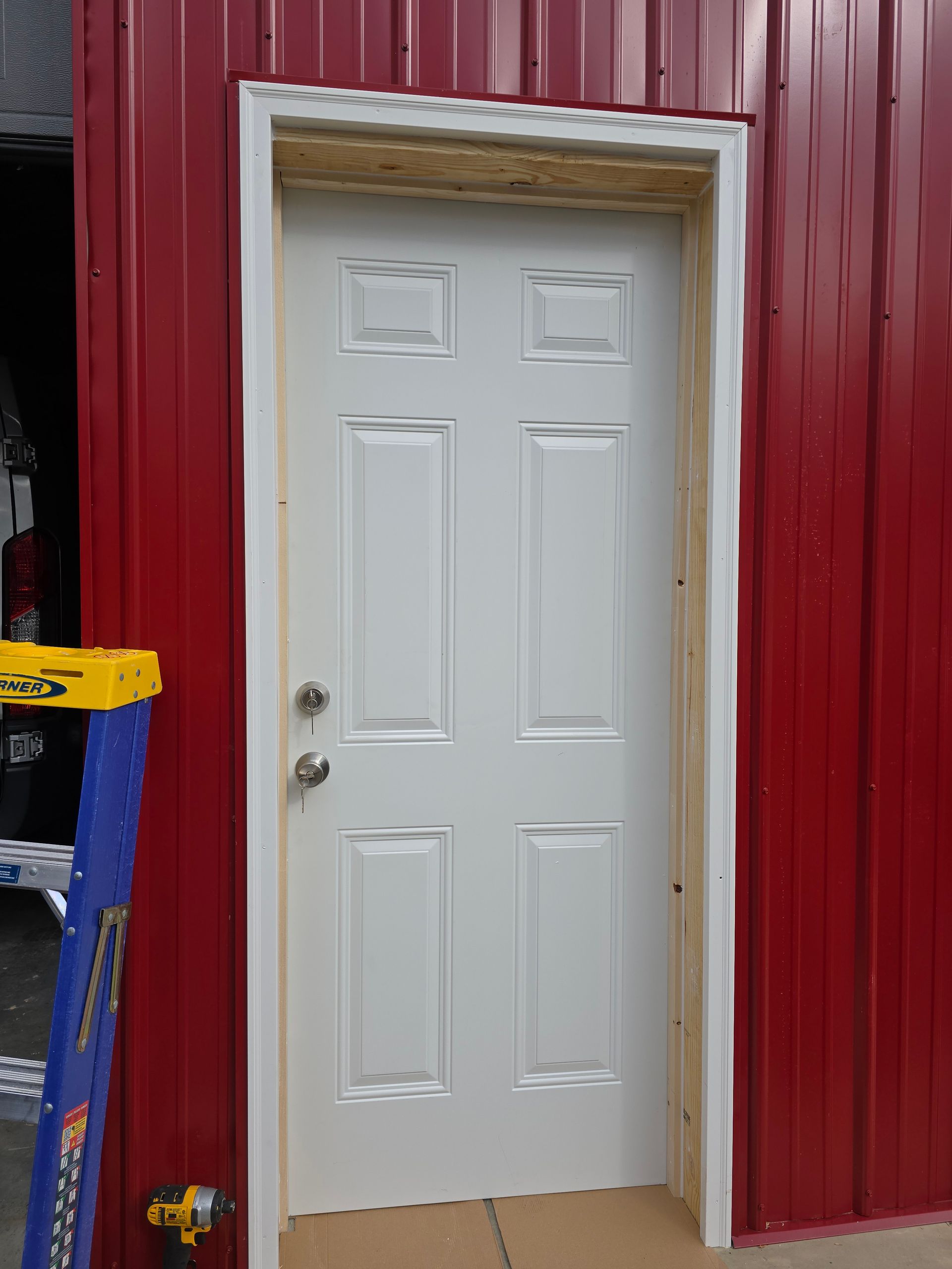 White door in a red metal building wall, with a small step and a blue ladder beside it.