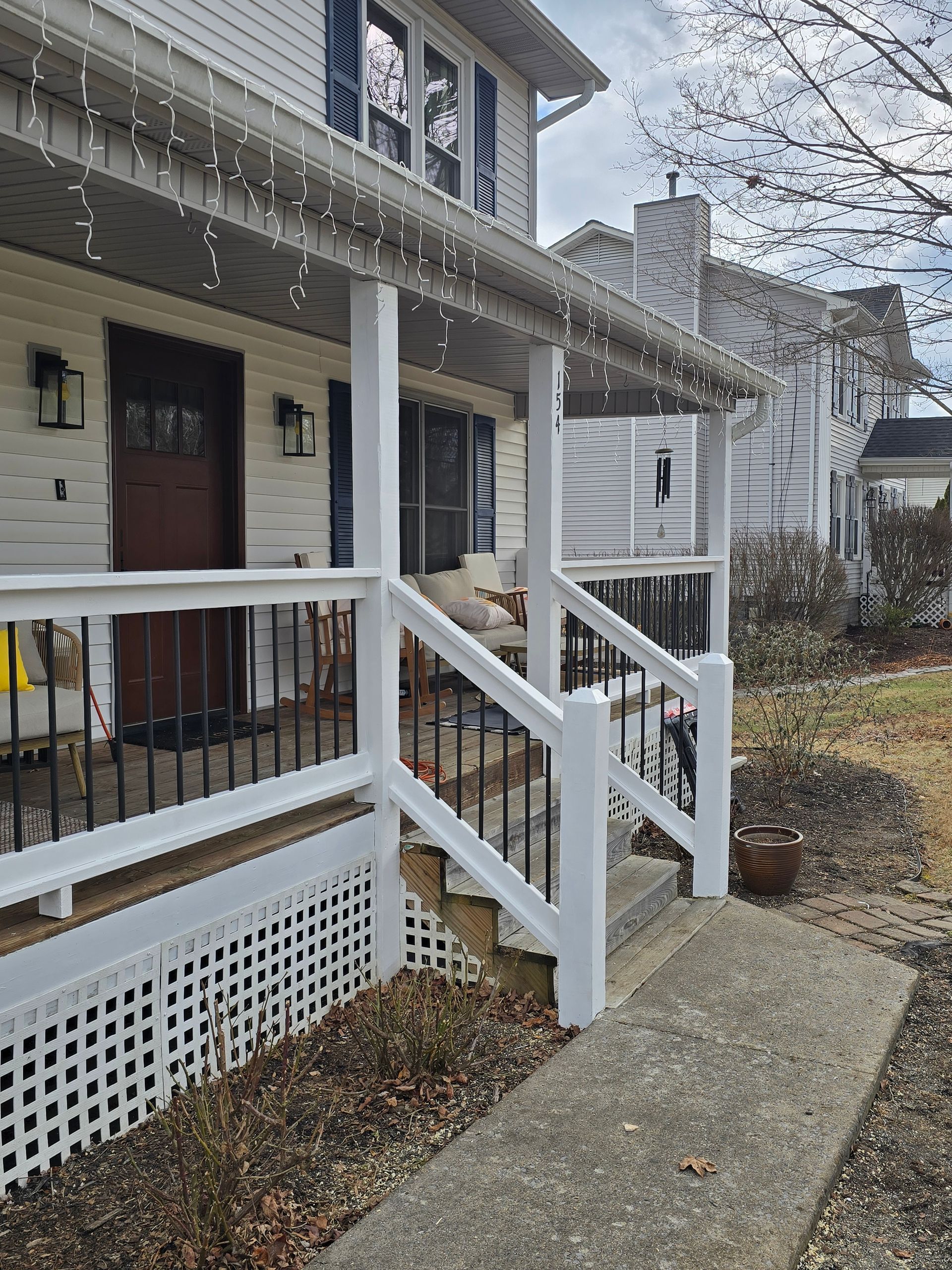 Front porch of a white house with string lights, steps, and a concrete walkway on a rainy day