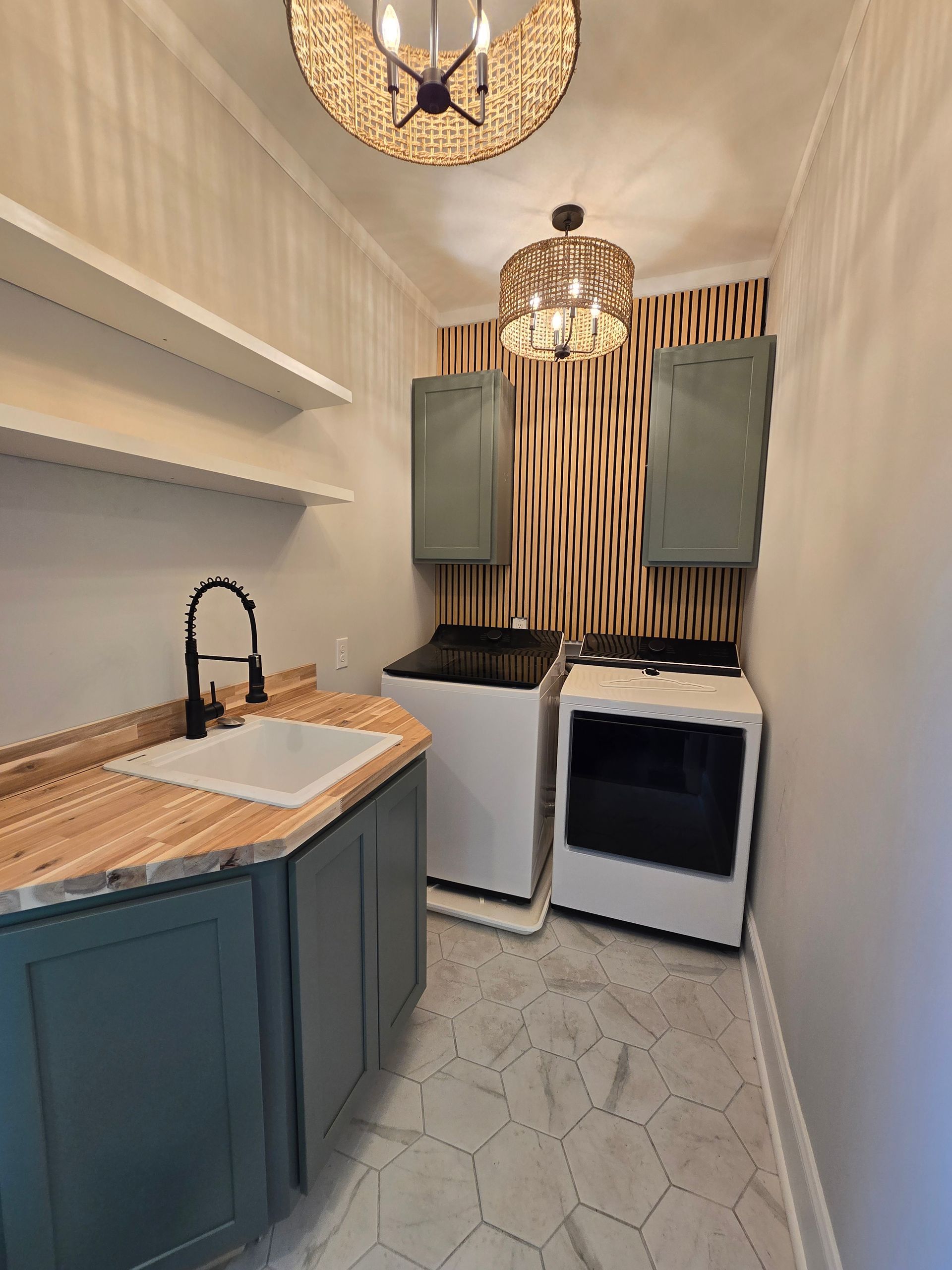Narrow laundry room with blue cabinets, wood countertop, sink, washer, dryer, and patterned floor under pendant lights
