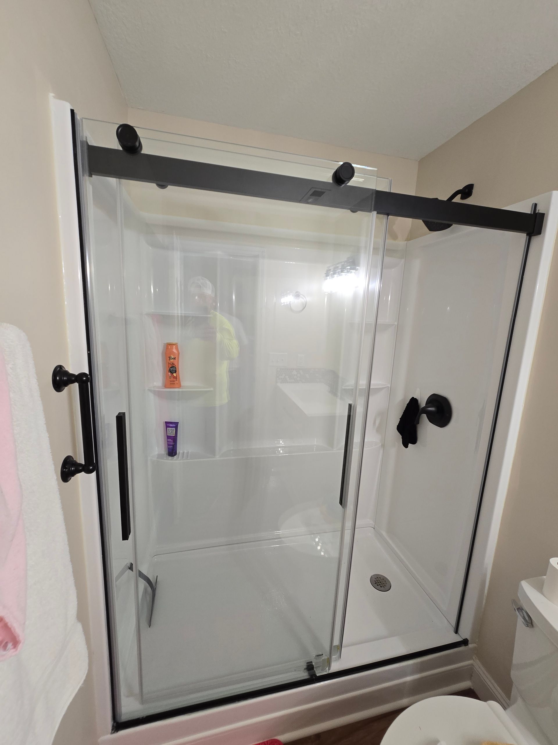 Glass shower enclosure with black hardware and a white bathroom interior