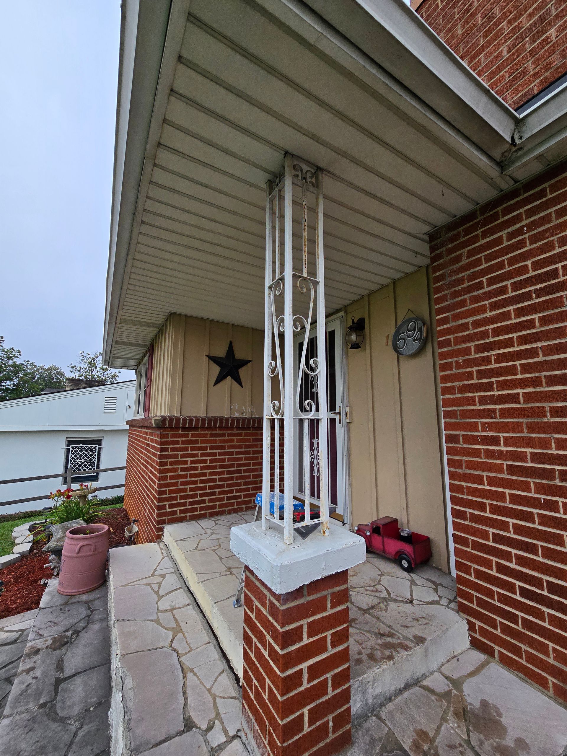 Front porch with brick columns, stone steps, and a hanging star decoration under a sloped roof.