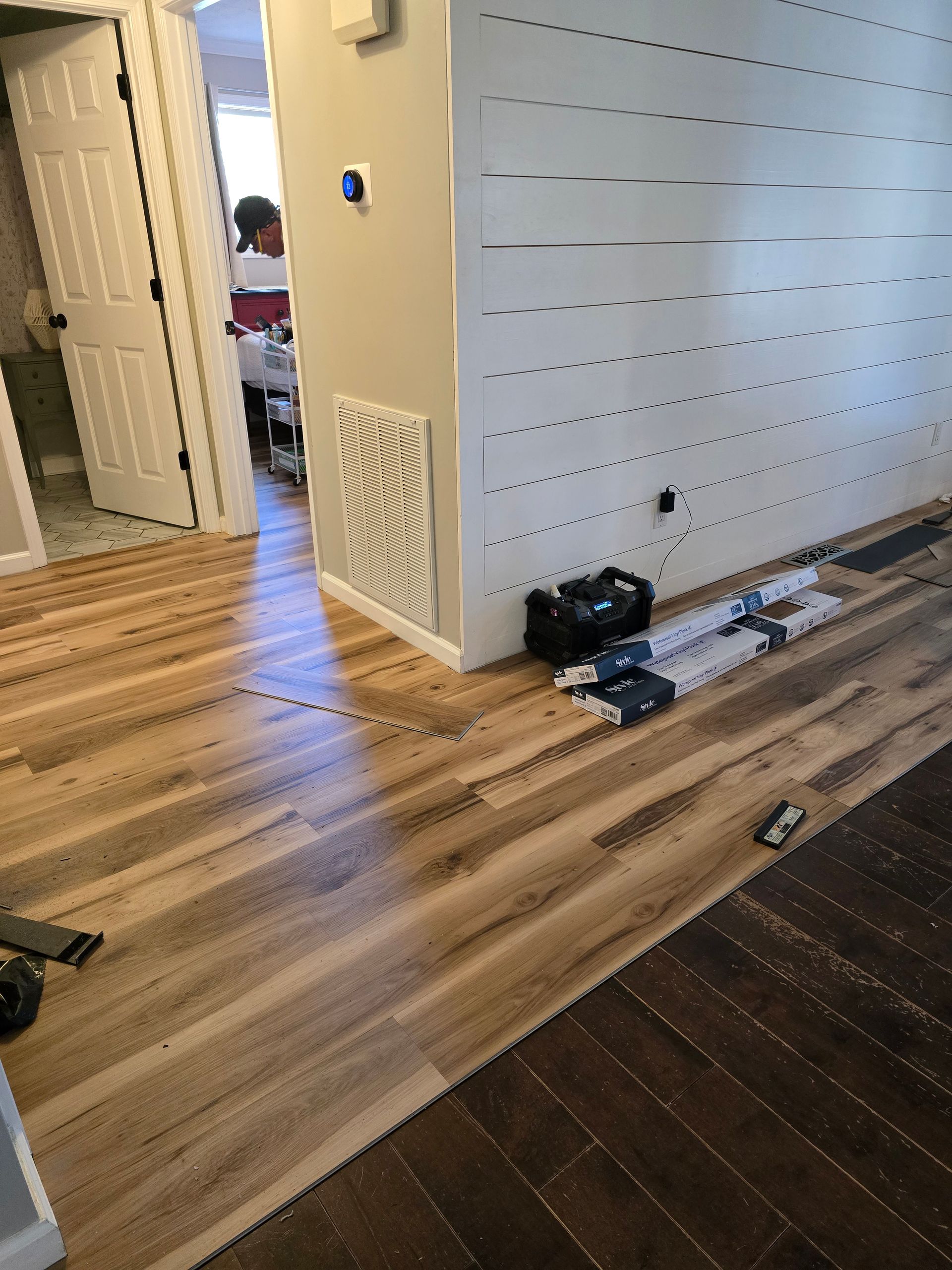 Hallway with wood floors, white walls, and a doorway; shoes and bags on the floor near a pegboard wall.