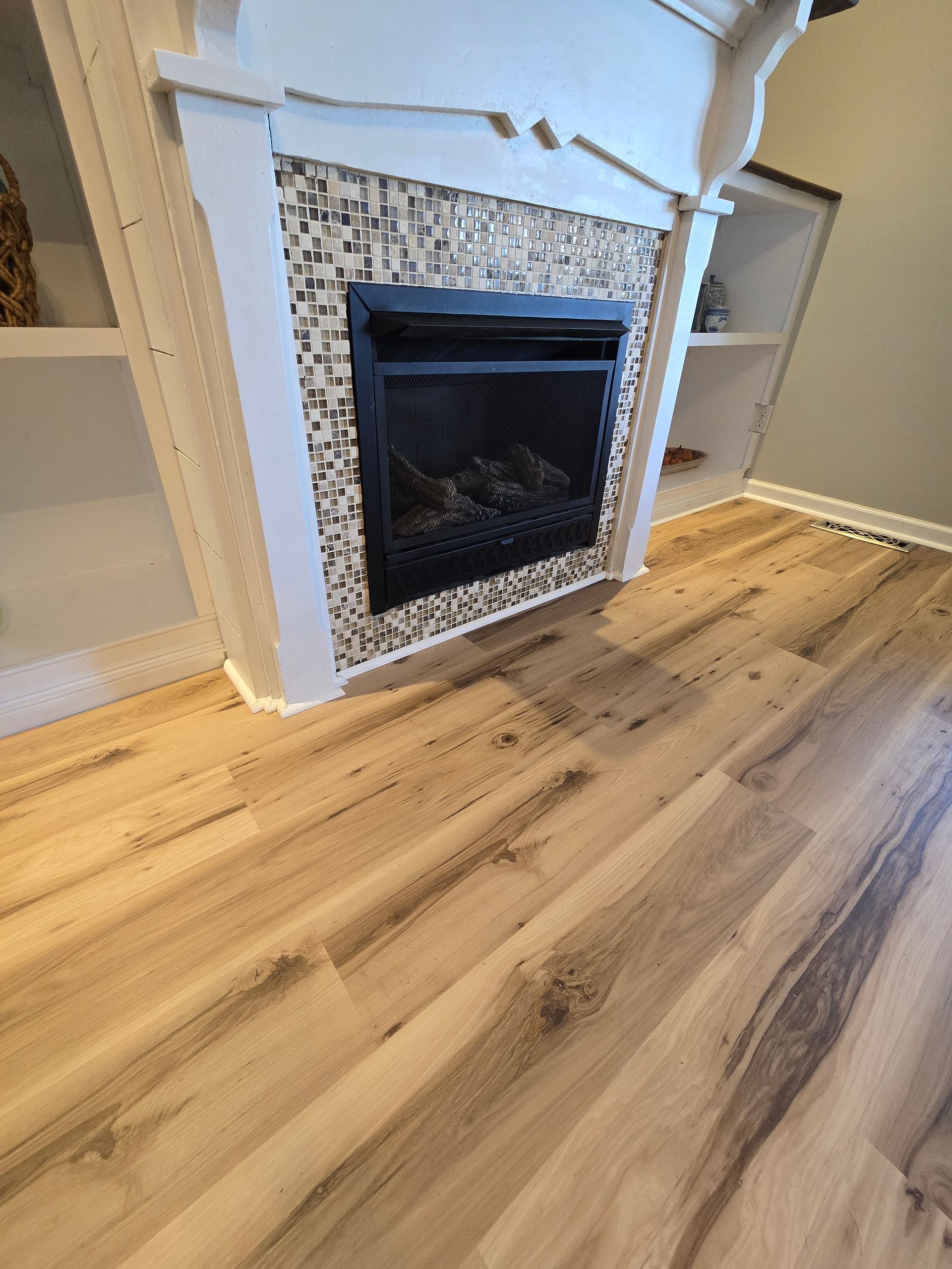 Modern living room fireplace with white mantel, mosaic tile surround, and wood flooring