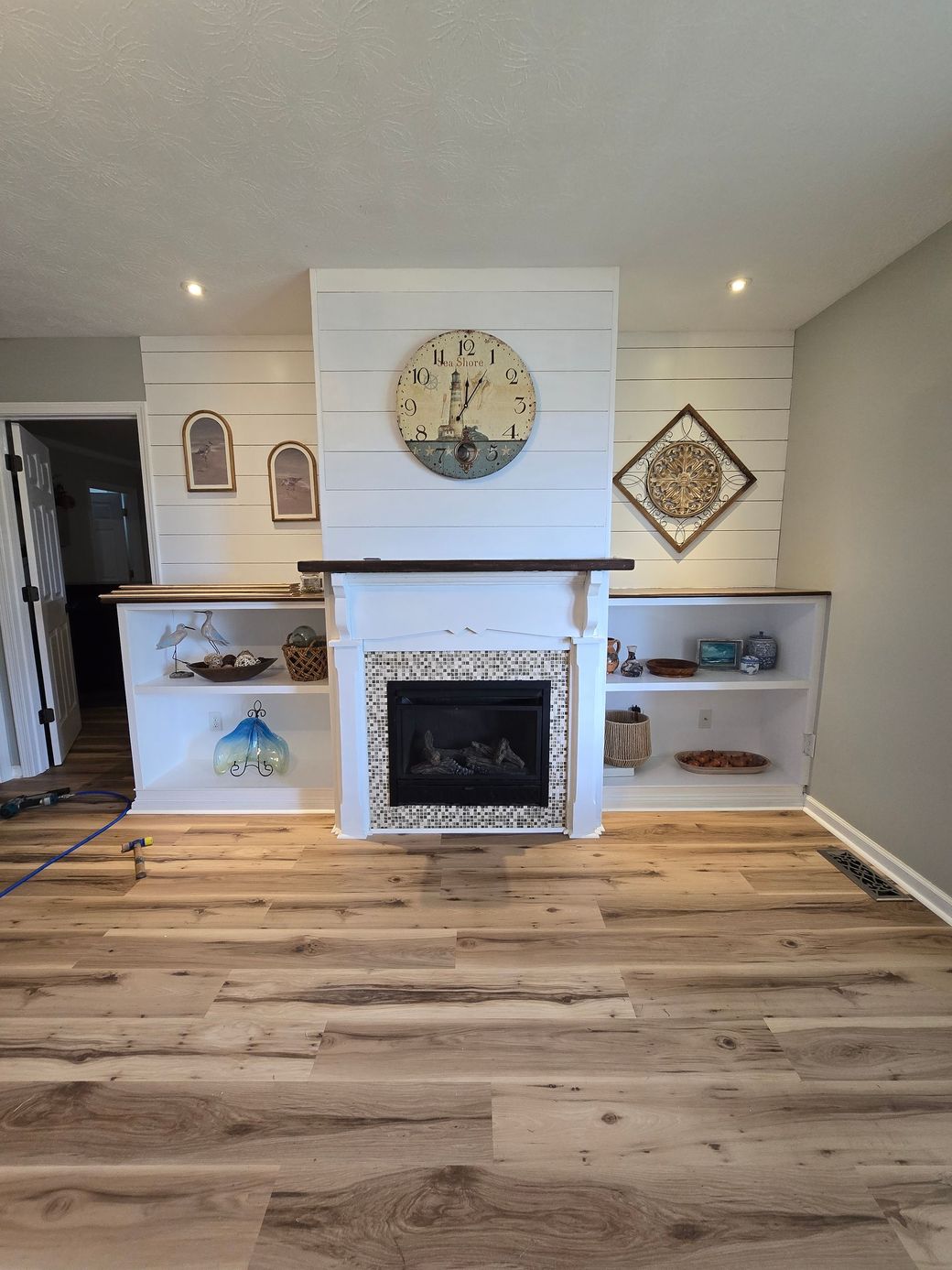 Living room with white fireplace, built-in shelves, large clock, and wood plank floor