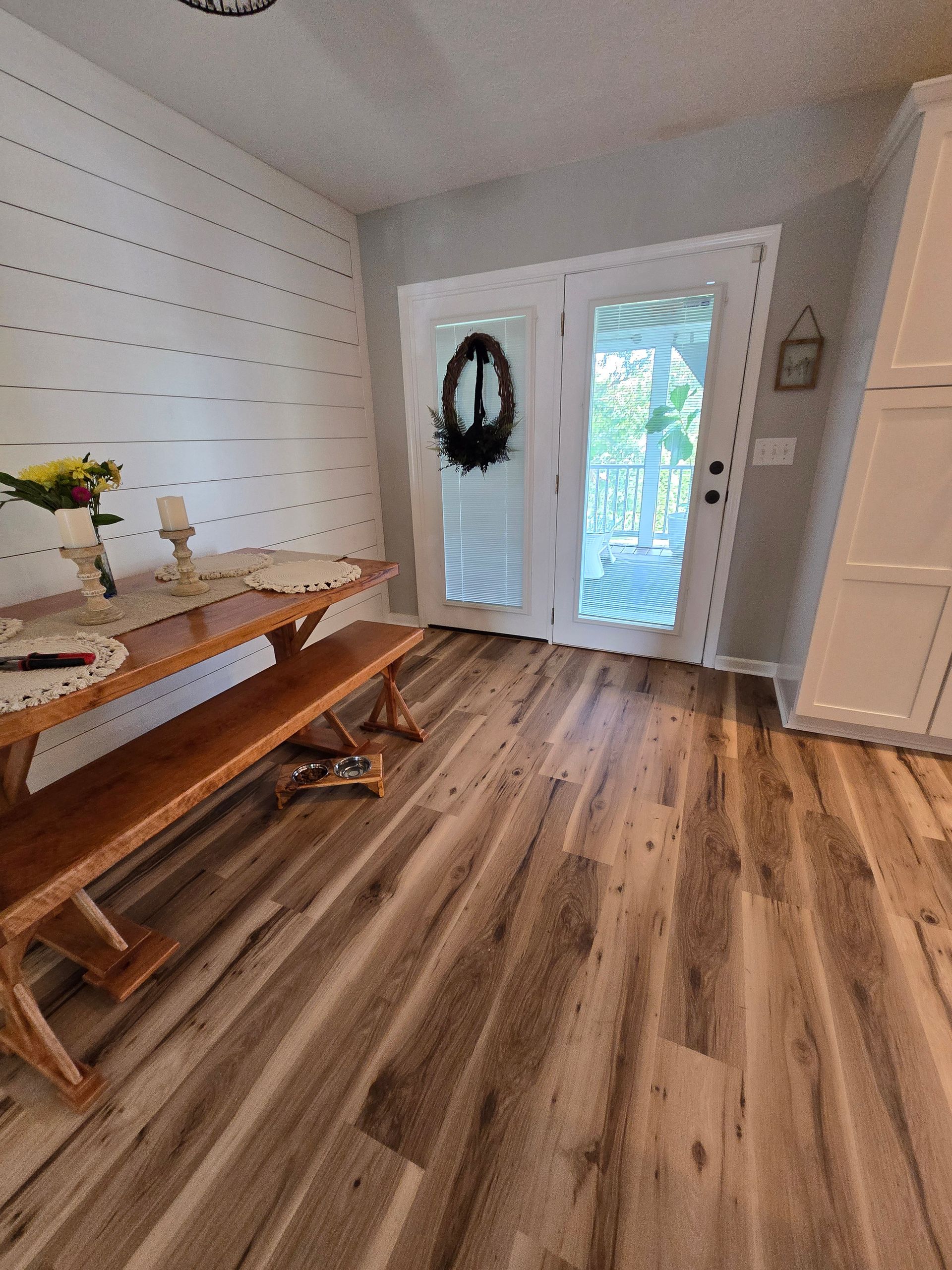 Bright entryway with wood floor, long wooden bench, white walls, and a front door with wreath and glass panel.