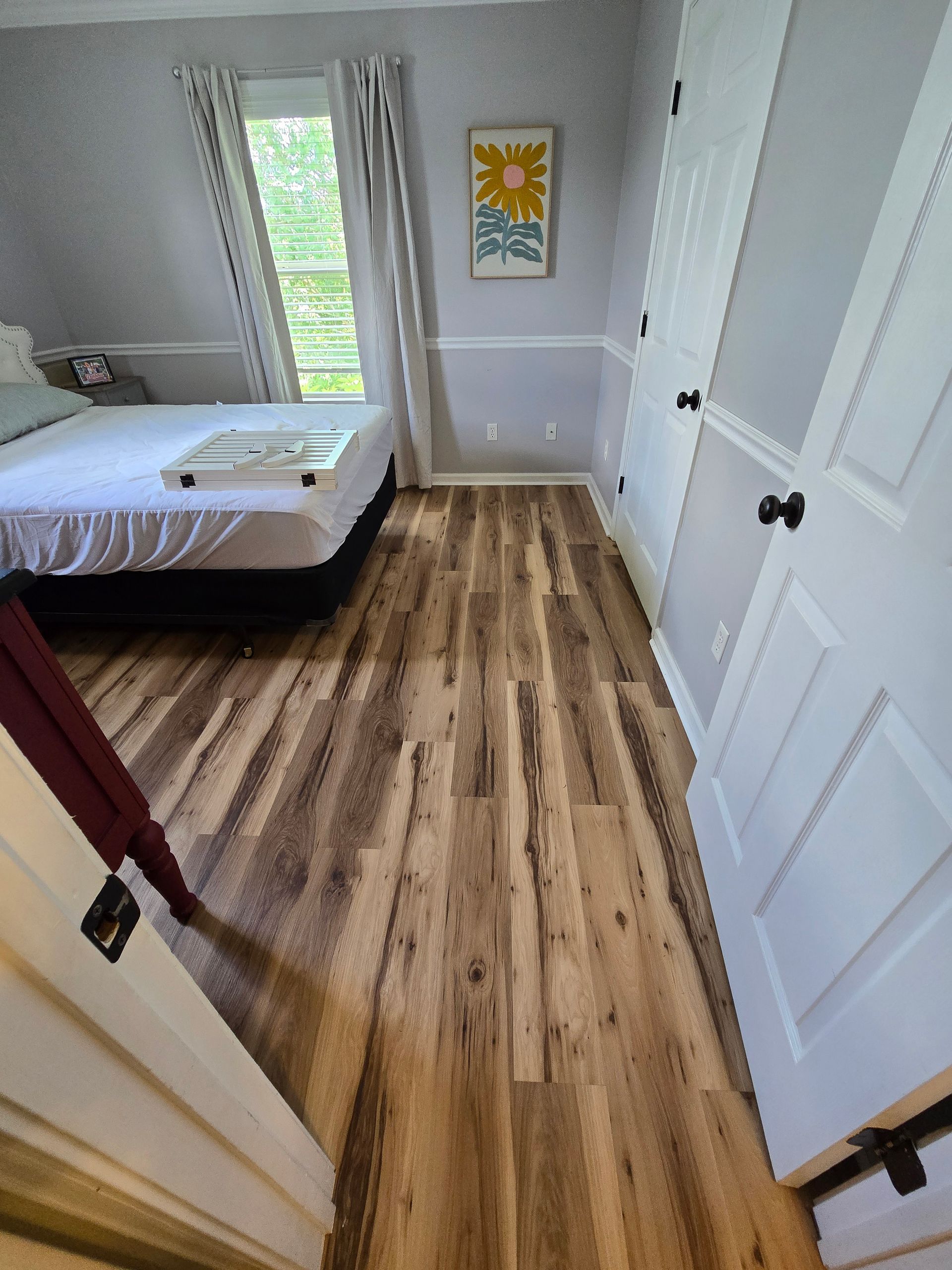 Small bedroom with bed, wood floor, white walls, and a window with curtains.