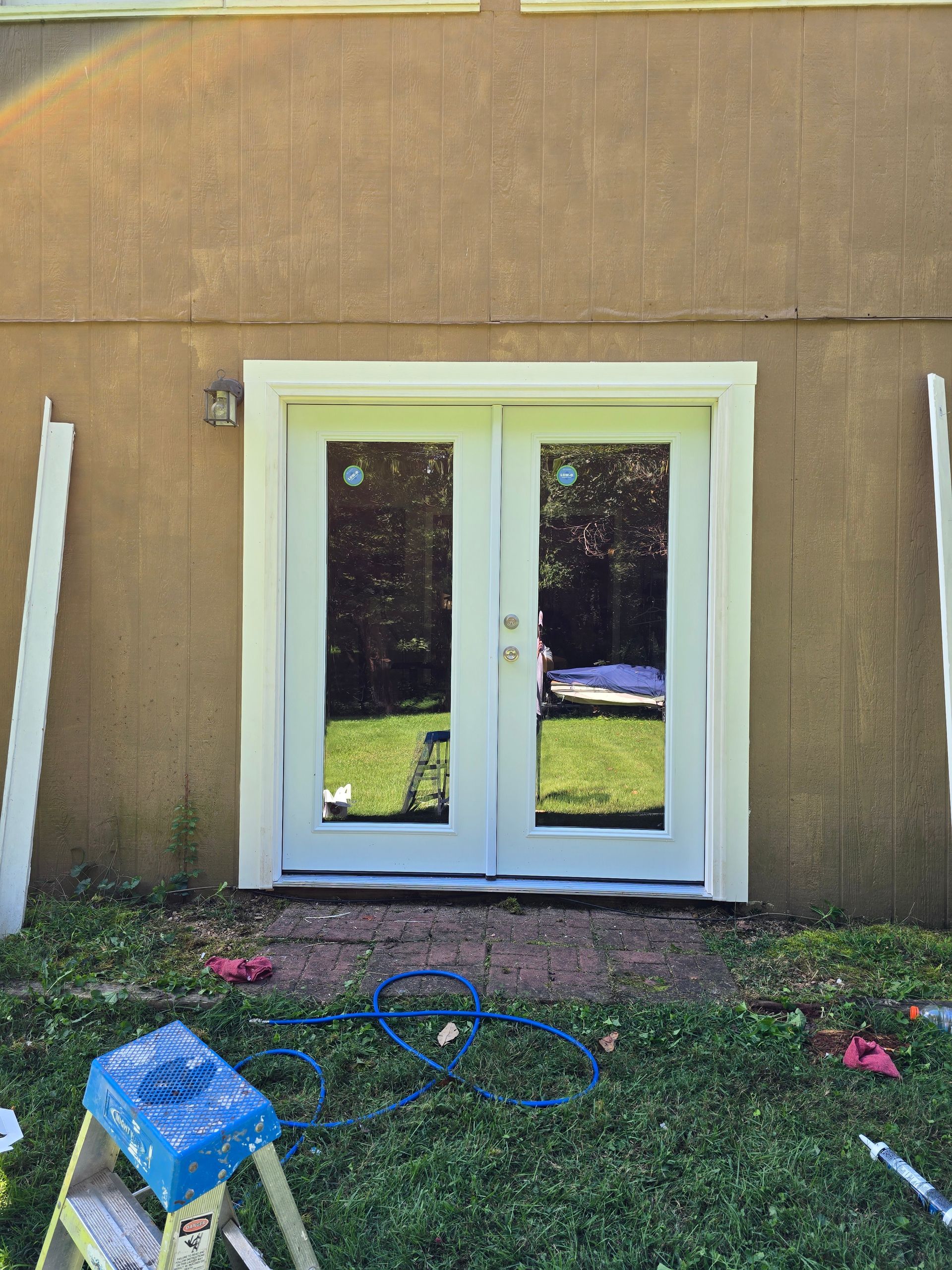 White double doors in a tan wall with a grassy yard and scattered tools in front