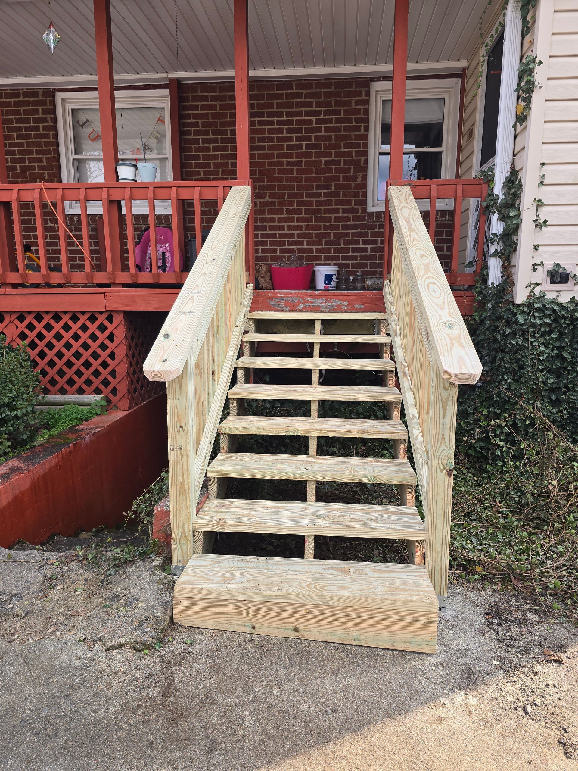 Exterior wooden staircase leading to a red brick porch with railings and diamond-plate landing