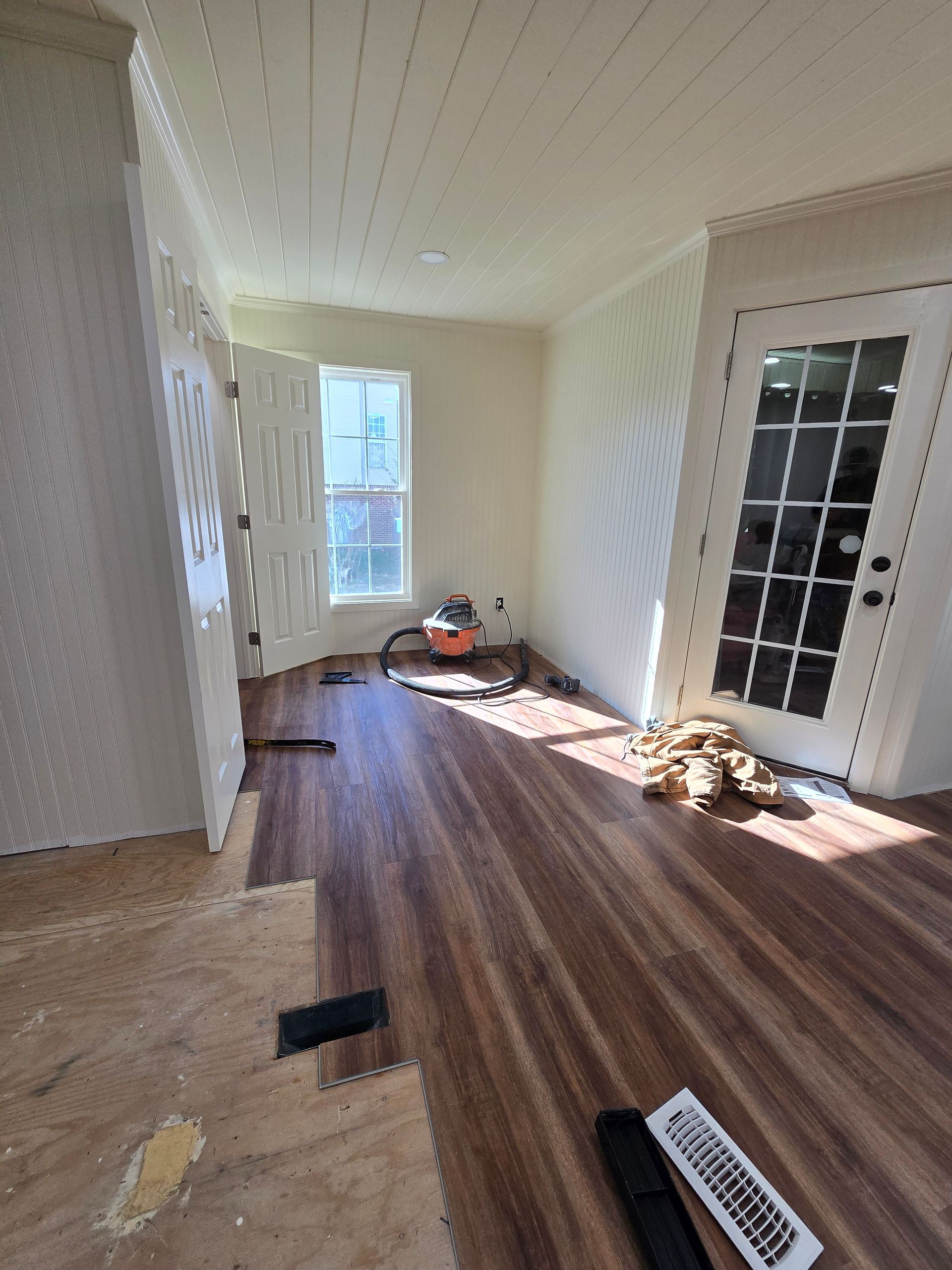 Empty room with wood floor, white walls, window, and French doors in a partially renovated interior