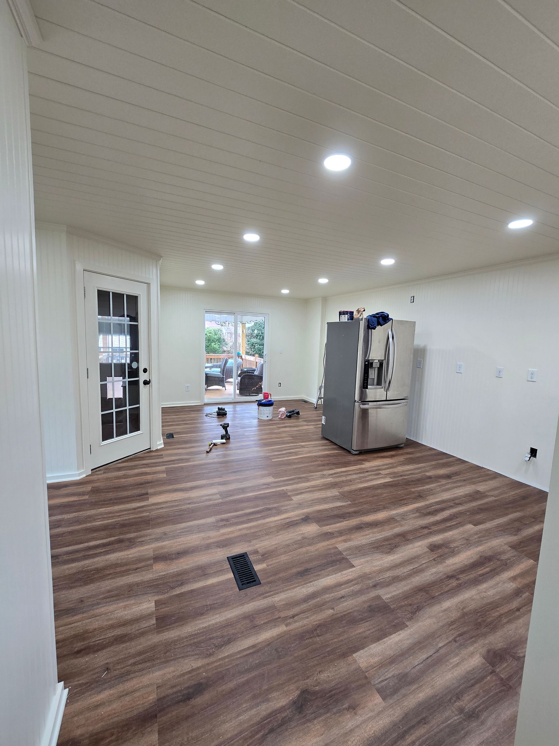 Empty room with wood-pattern floor, white walls, recessed lights, and a stainless steel refrigerator.