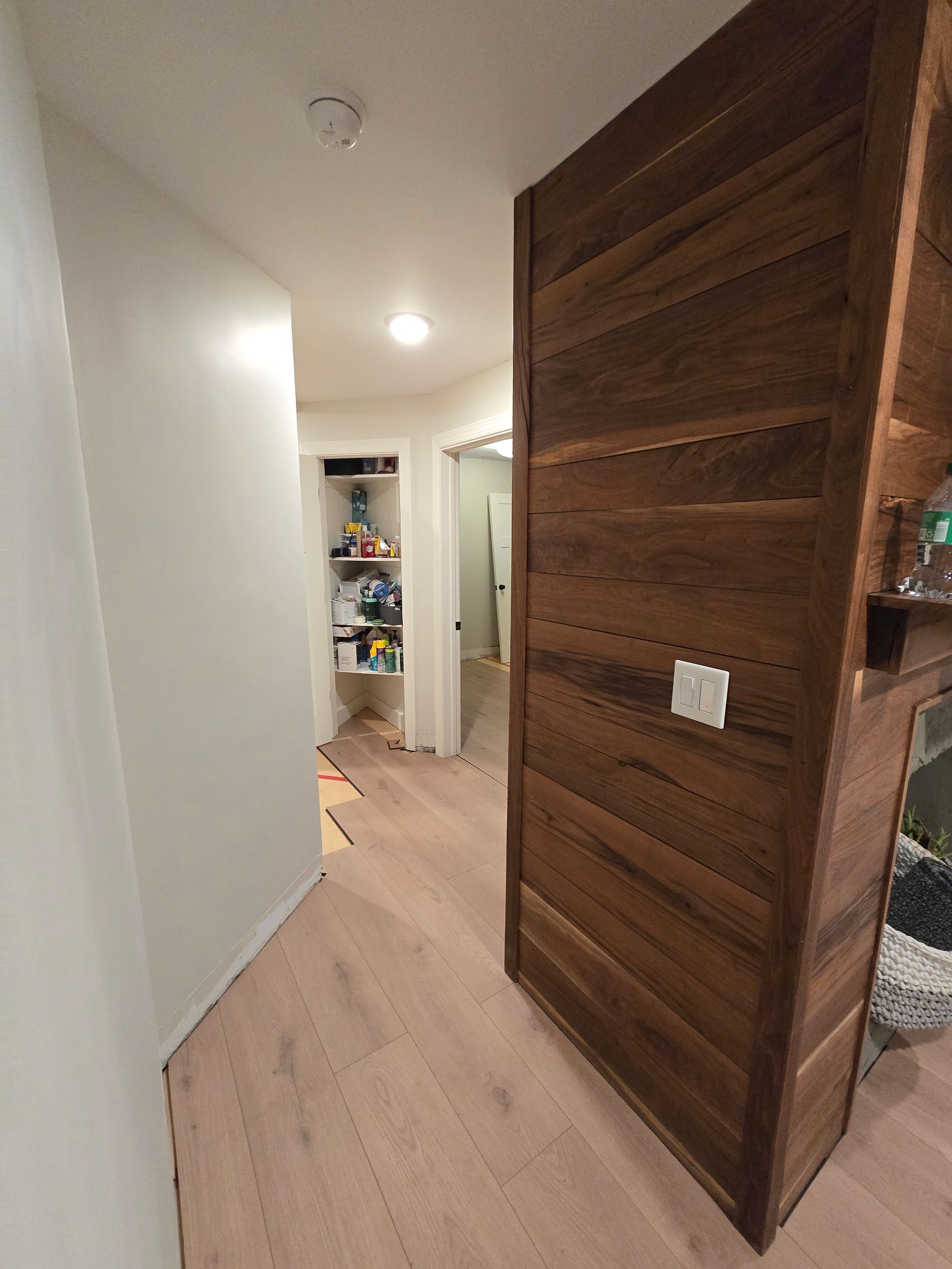 Narrow hallway with white walls, light wood floor, and a partially open dark wood door at right.
