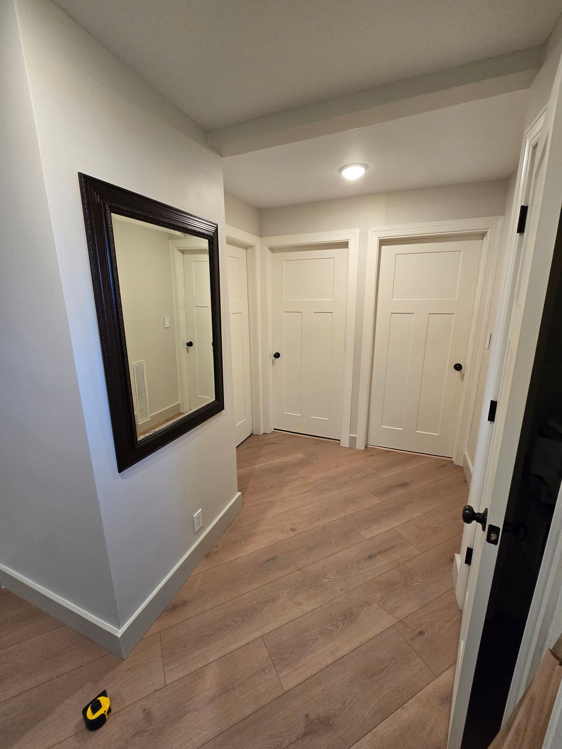 Empty hallway with white doors, wall mirror, and wood flooring.