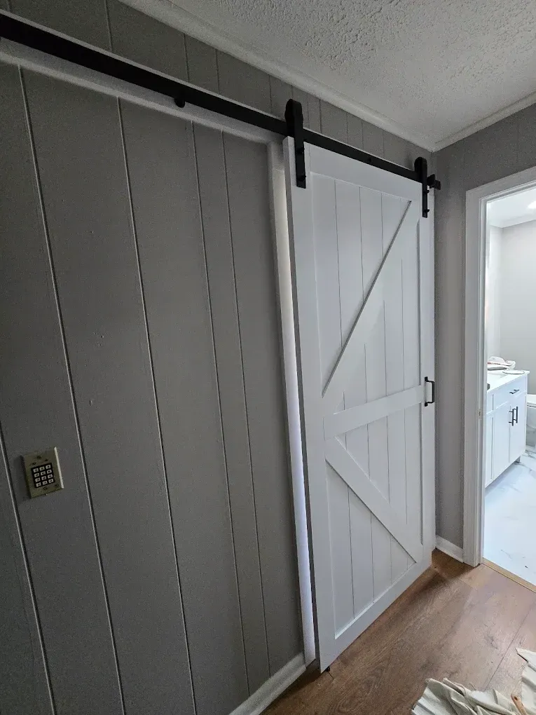 White barn-style sliding door in a hallway beside an open doorway to a bright kitchen.