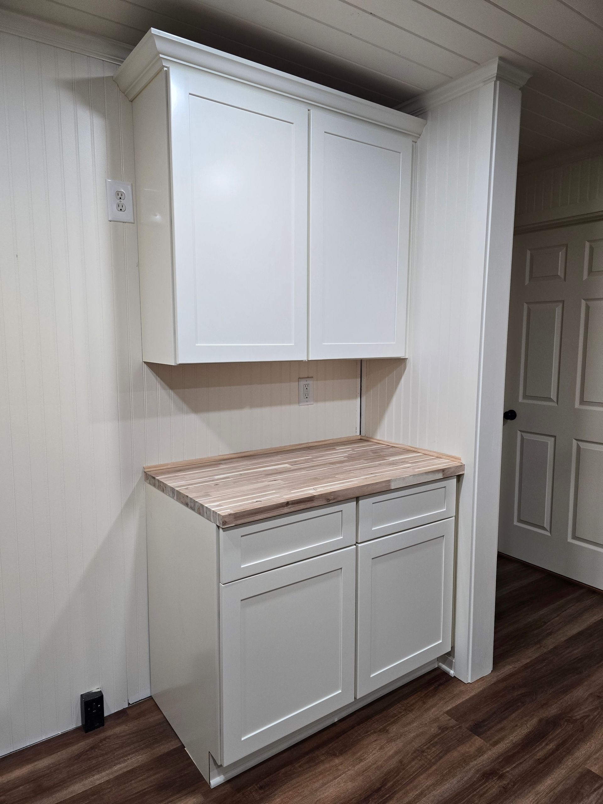 White wall cabinets above and below a speckled countertop in a hallway nook with wood flooring