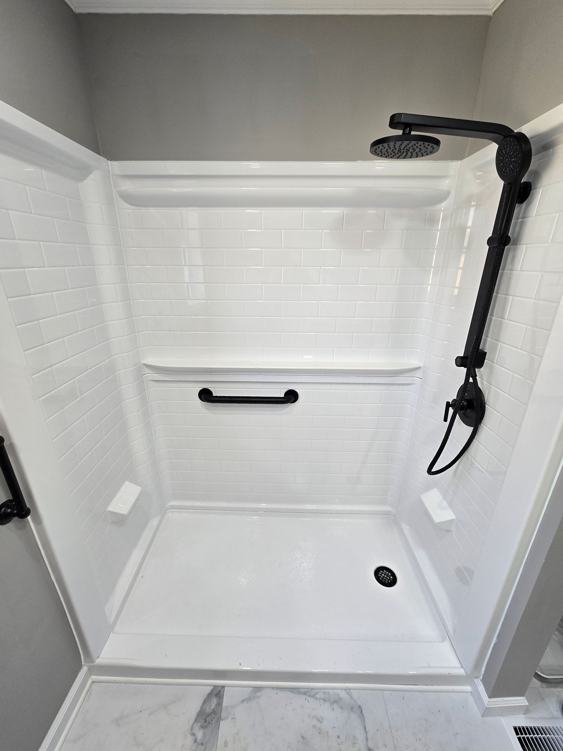 White walk-in shower with bench, grab bars, and handheld showerhead.