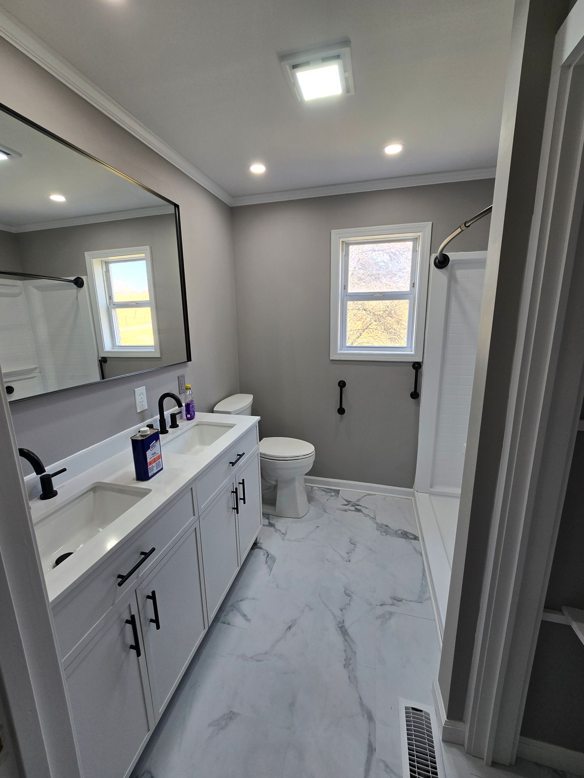Modern bathroom with white vanity, large mirror, tiled floor, and small window.