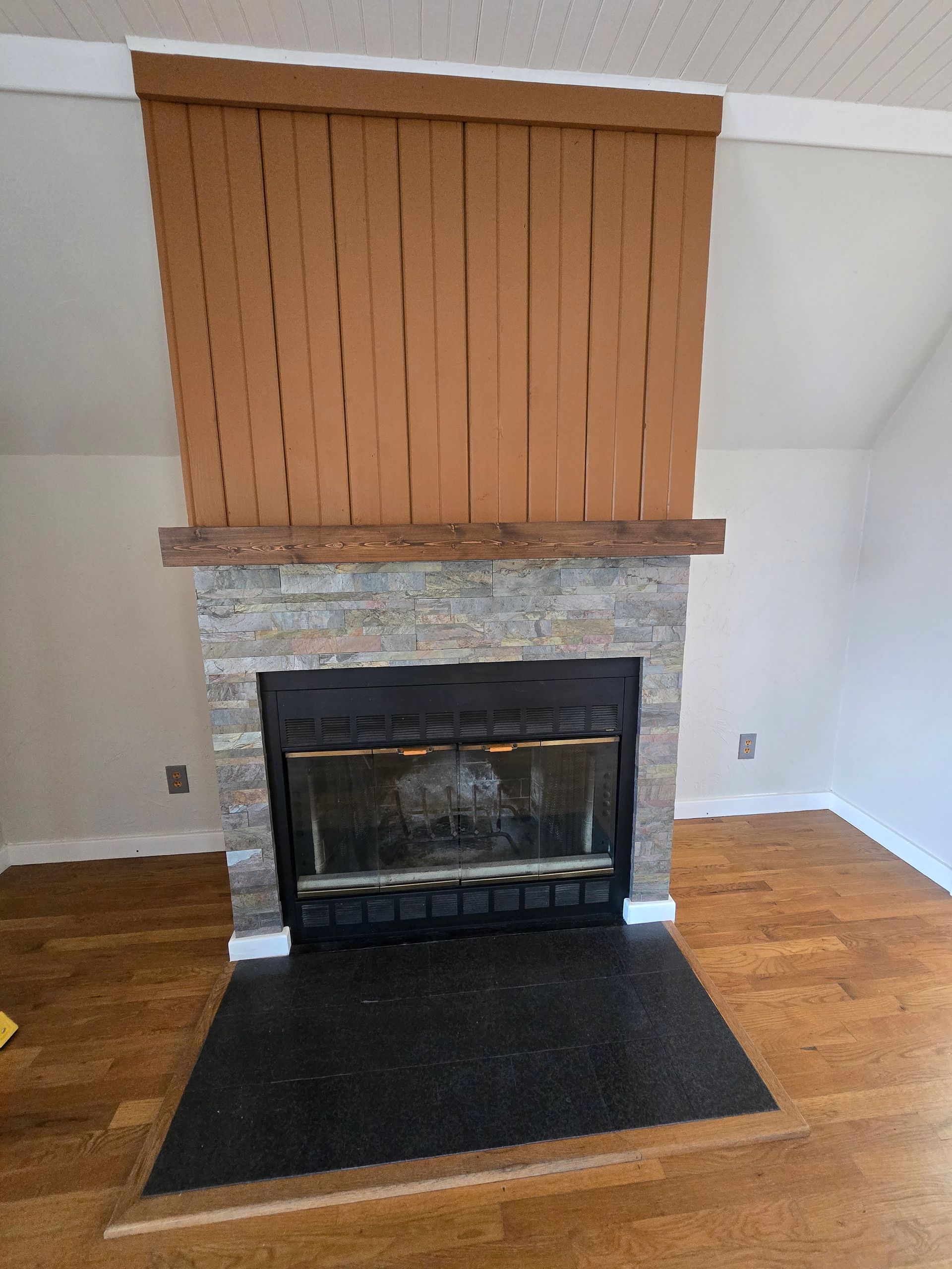 Stone fireplace with black hearth and tan wood paneling above it in a living room.