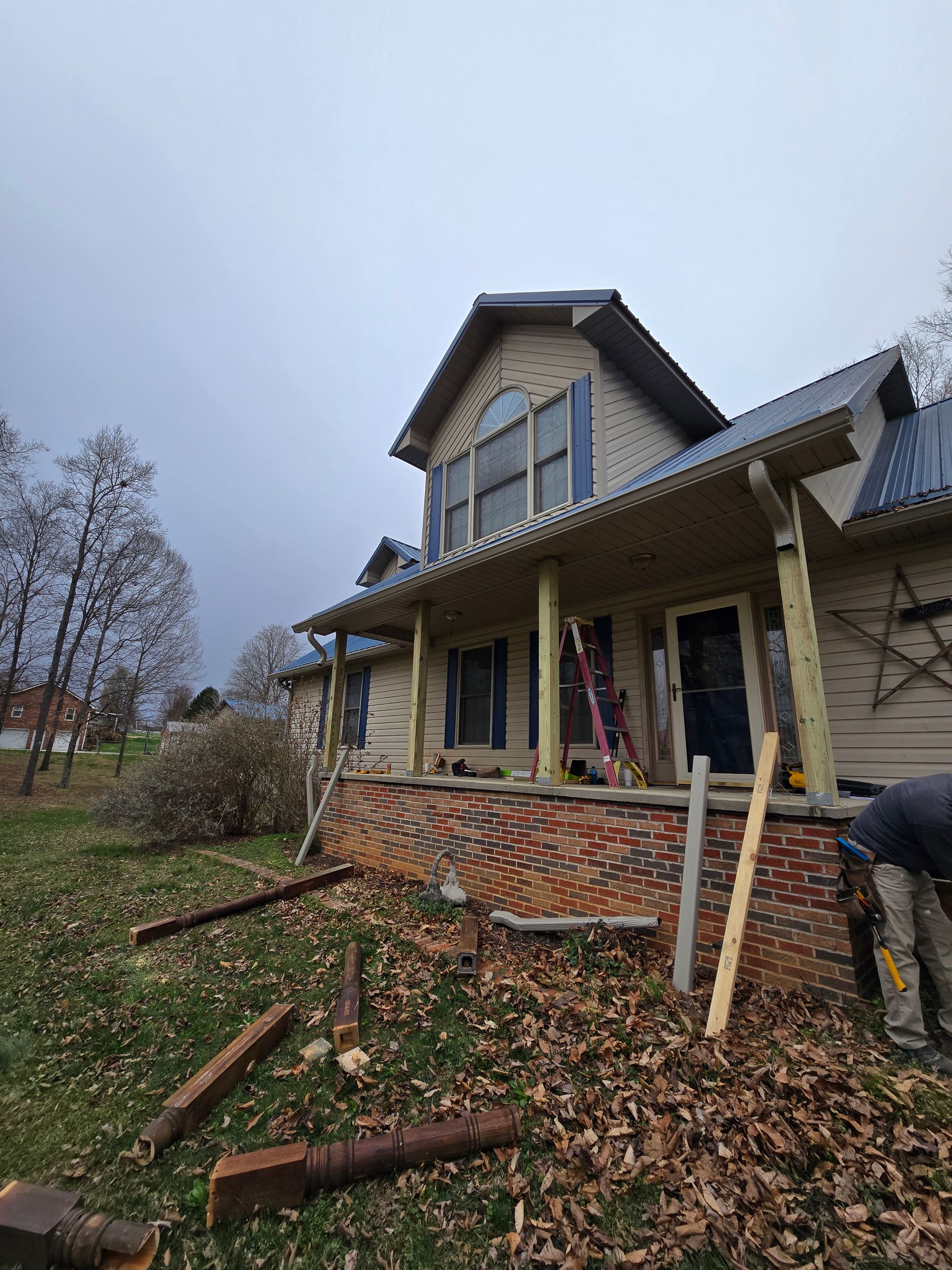 House with porch under renovation, with stacks of bricks and boards in a leaf-covered yard