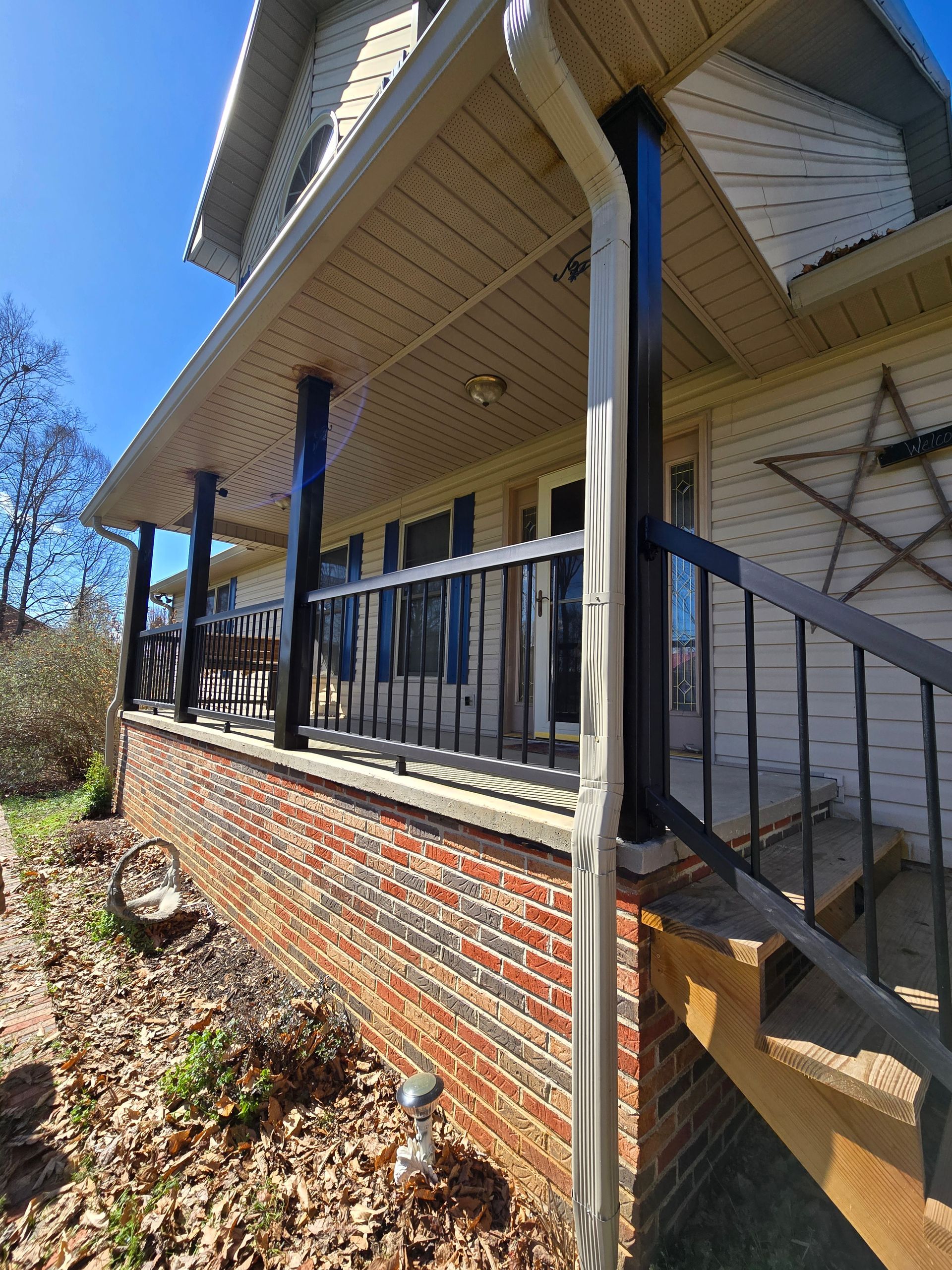 Brick porch with black railings and steps on a house exterior, viewed from below.