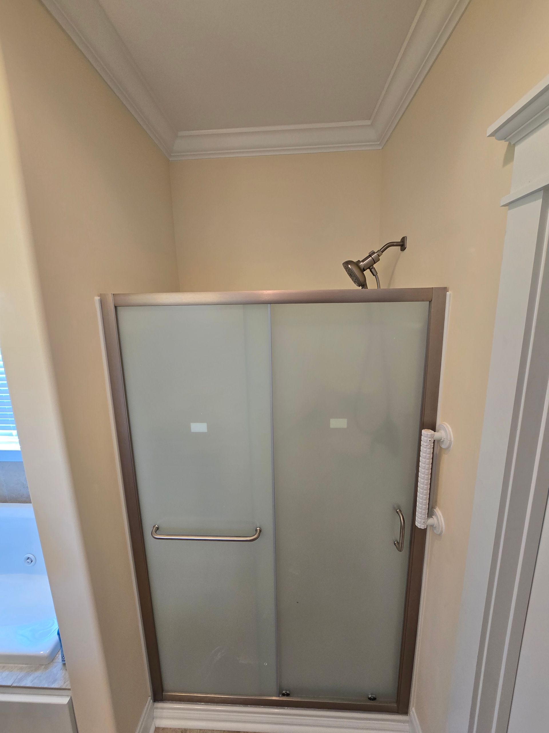 Frosted glass shower enclosure in a beige bathroom corner with a wall-mounted showerhead.