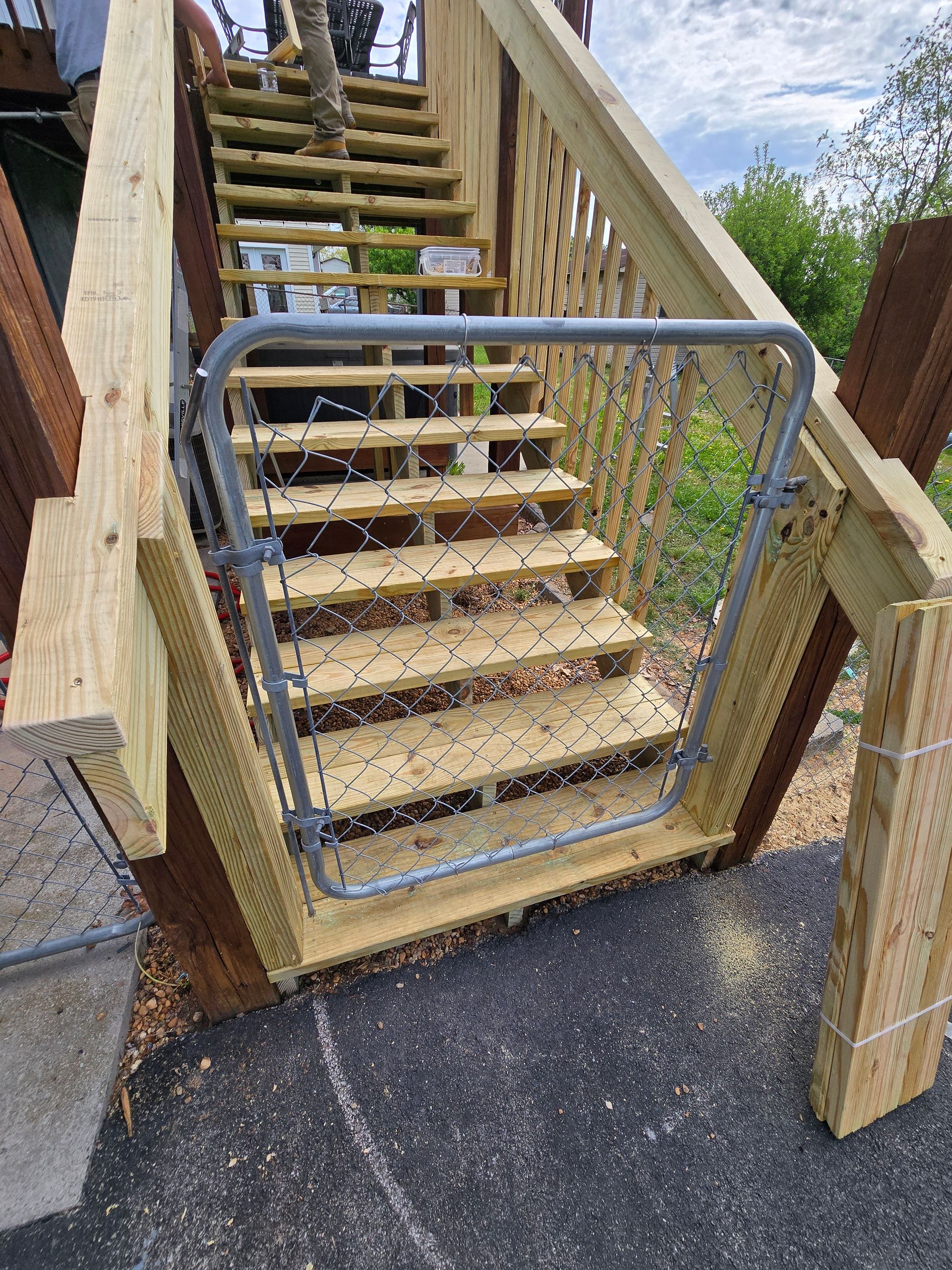 Wooden outdoor stairs with a closed metal gate and gravel path at the base
