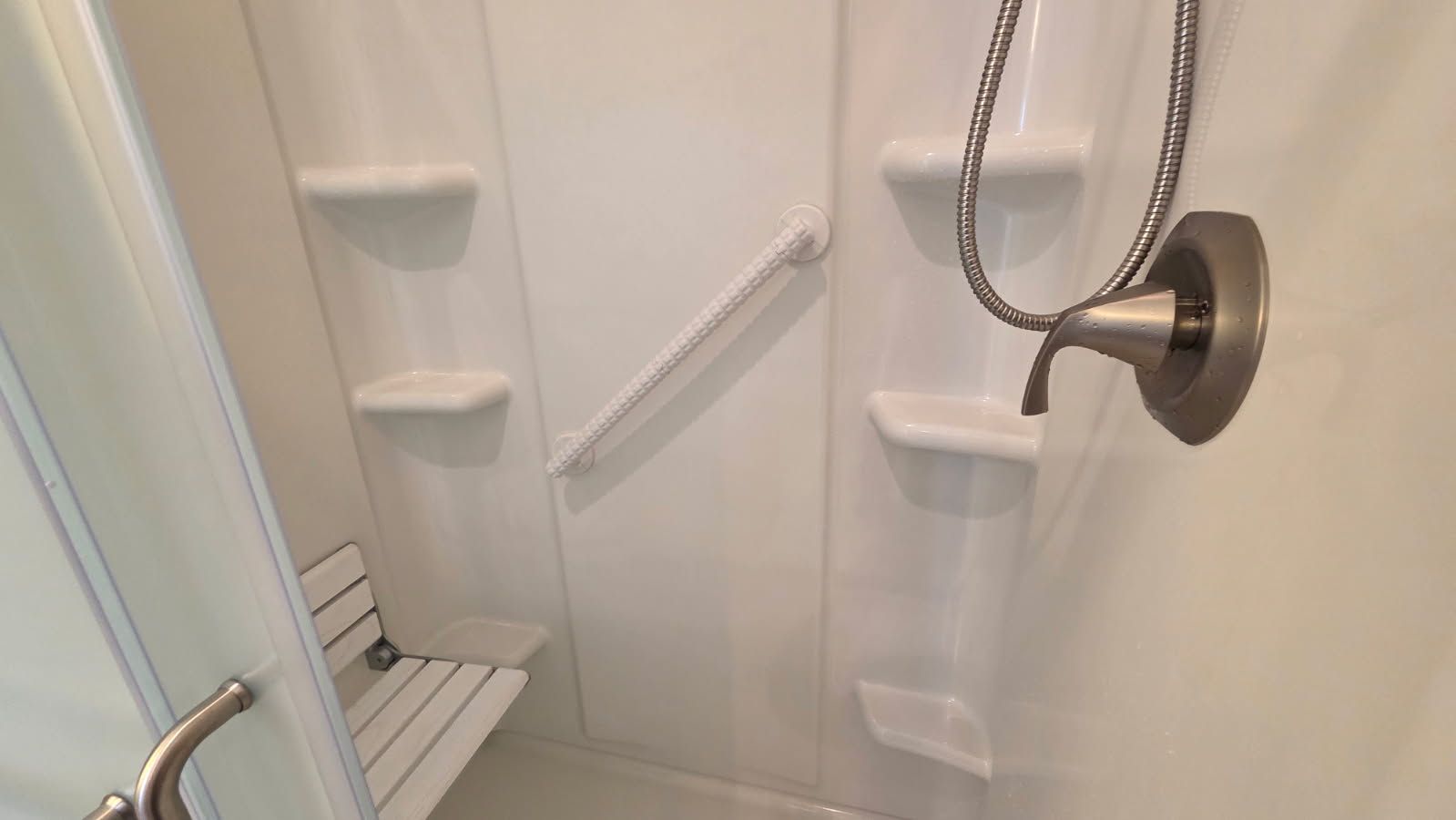 Shower stall with white tiled walls, built-in shelves, and a showerhead with a handheld hose.