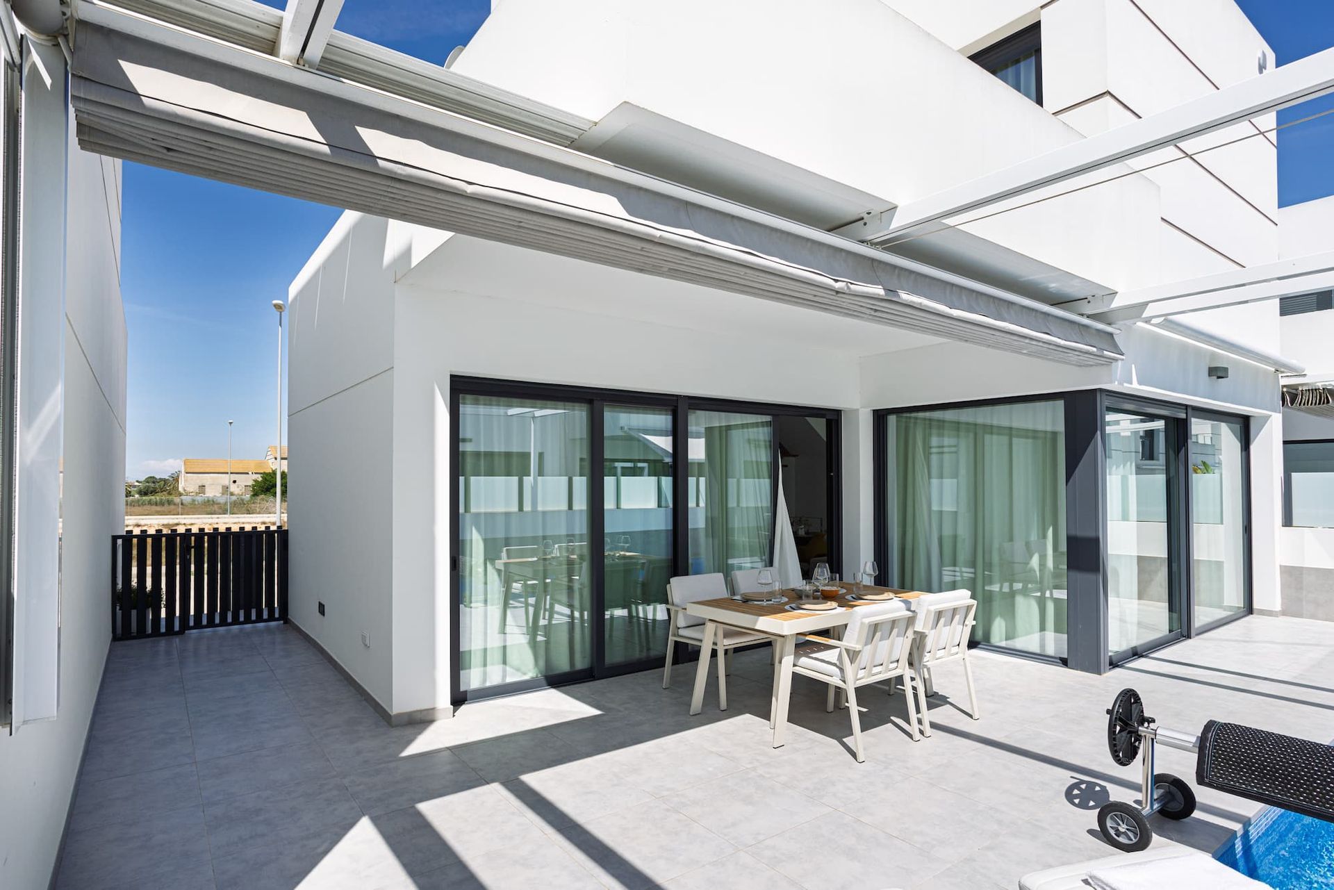 Modern white home exterior with patio, outdoor dining set, and partial pool view.
