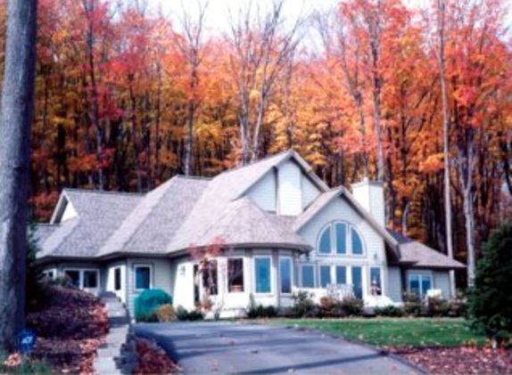 House with gray roof, surrounded by colorful autumn trees; driveway in front.