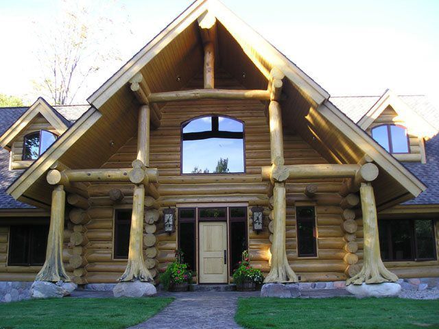 Log cabin home with large timber entryway, arched window, and landscaped yard.
