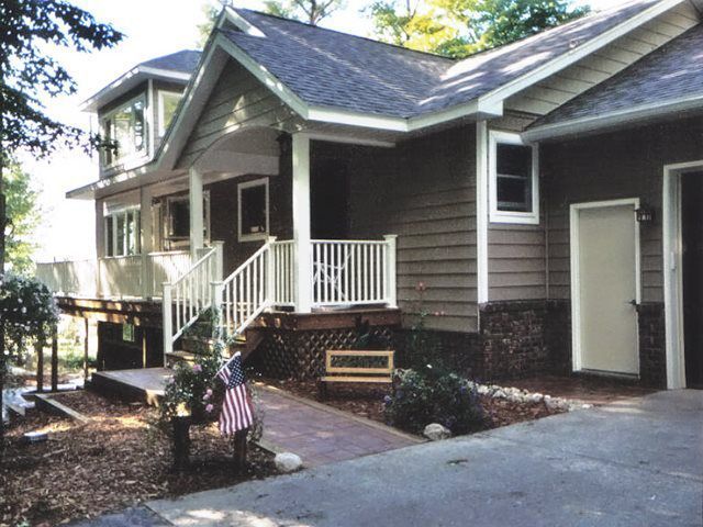 Brown two-story house with porch and deck, brick path, American flag, and garage.