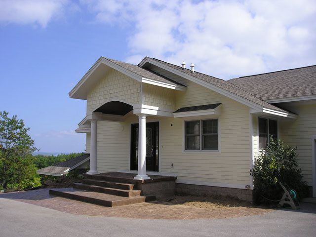 Beige house with porch, steps, columns, windows; blue sky background.