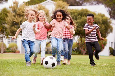 Children playing soccer on a grassy lawn; smiling, running toward the camera.
