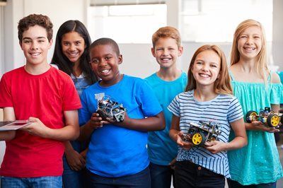 Group of children smiling, holding robots, possibly in a classroom or workshop setting.