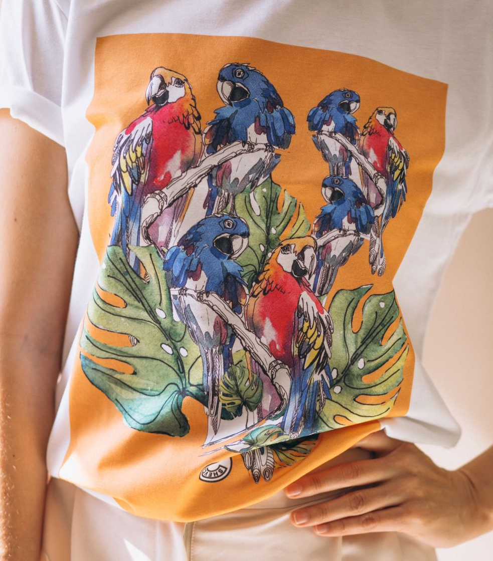 White t-shirt with DTF (Direct To Film) printed orange square print of colorful parrots on branches and green leaves.