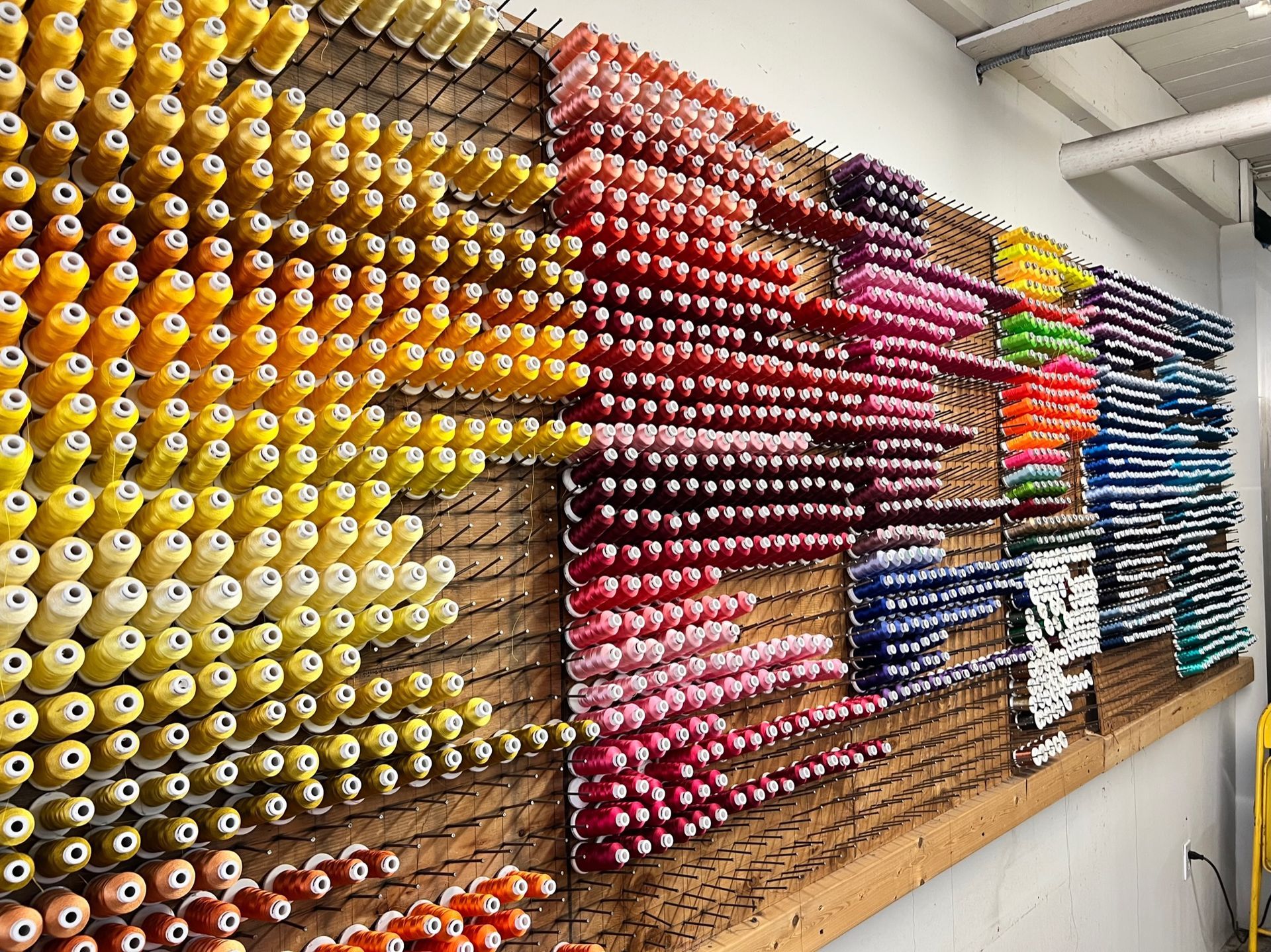 A wall-mounted display rack holds hundreds of spools of thread organized in a spectrum of colors.