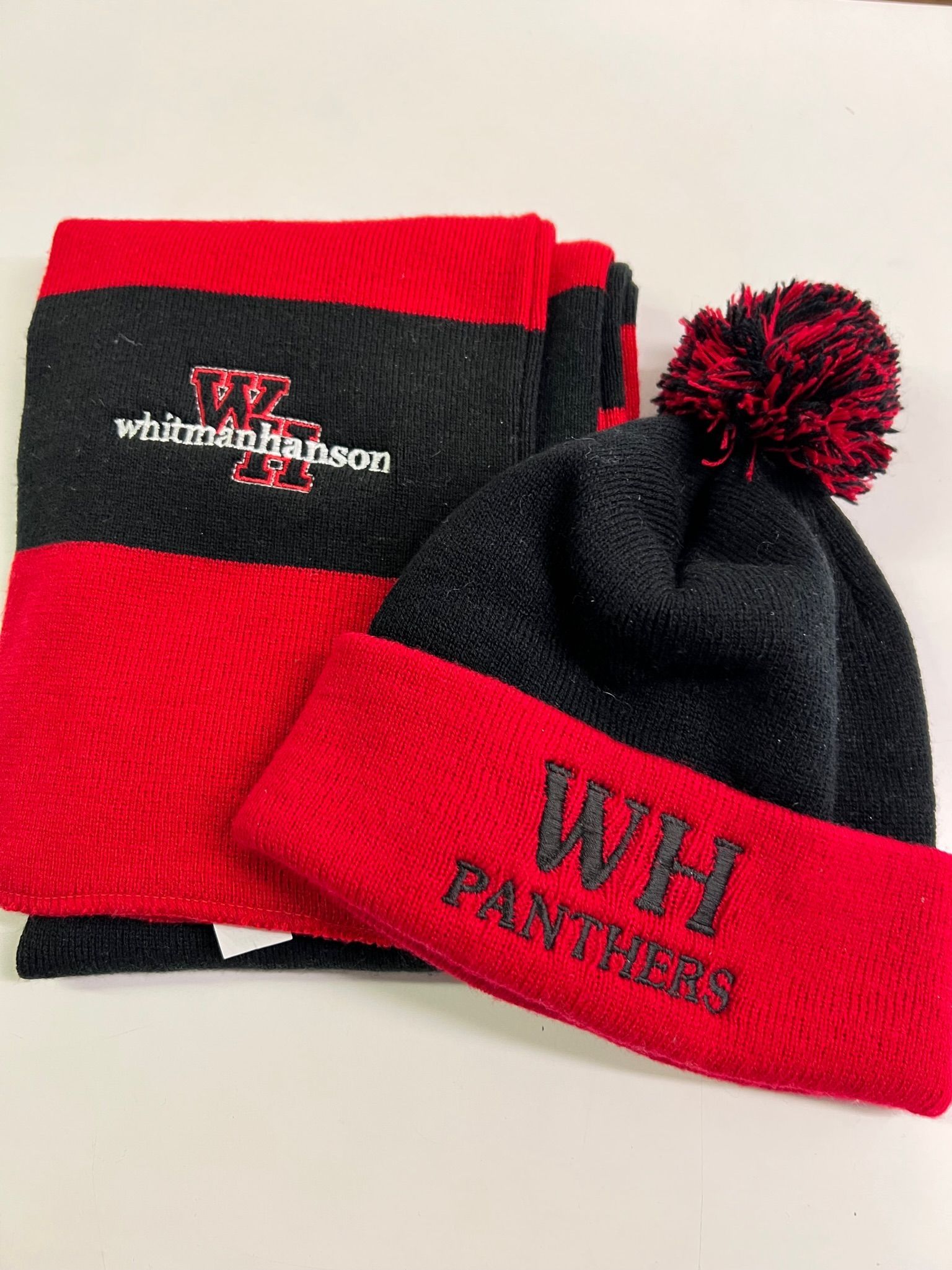 A black and red knit scarf and matching beanie with a pom-pom, featuring