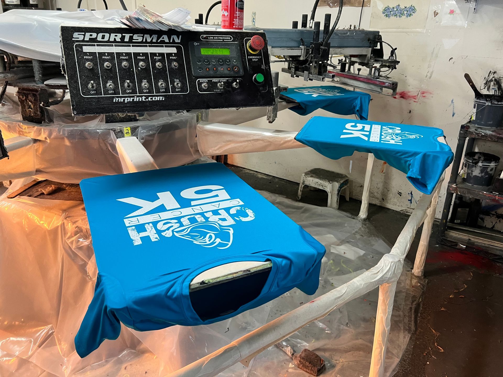 Blue t-shirts with custom silk screened white print on a screen printing machine in a workshop.