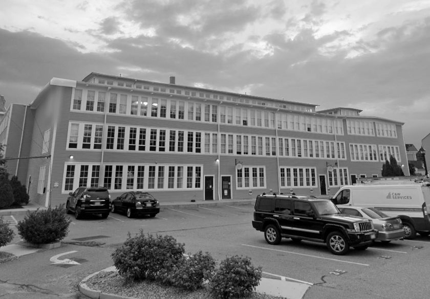 A multi-story commercial or school building with many rows of windows, set against a cloudy sky with cars in the lot.