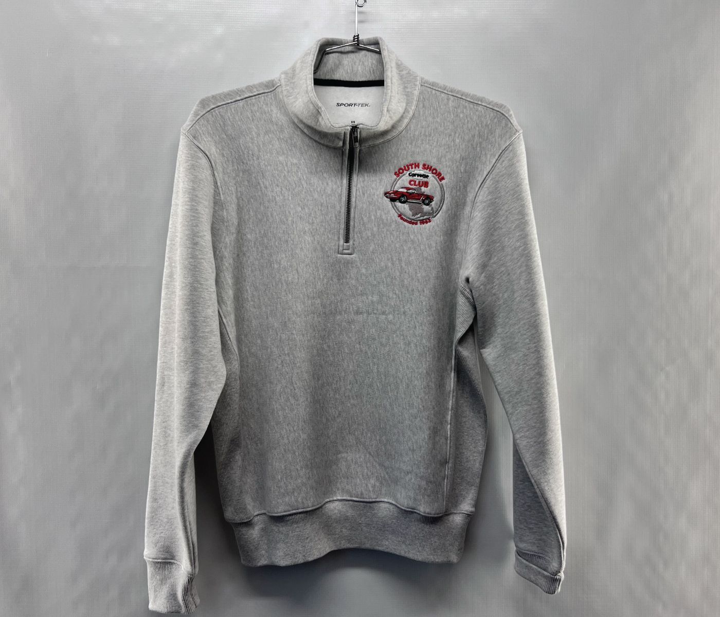 Gray quarter-zip sweater with a small red embroidered logo on the upper left chest, displayed on a hanger.