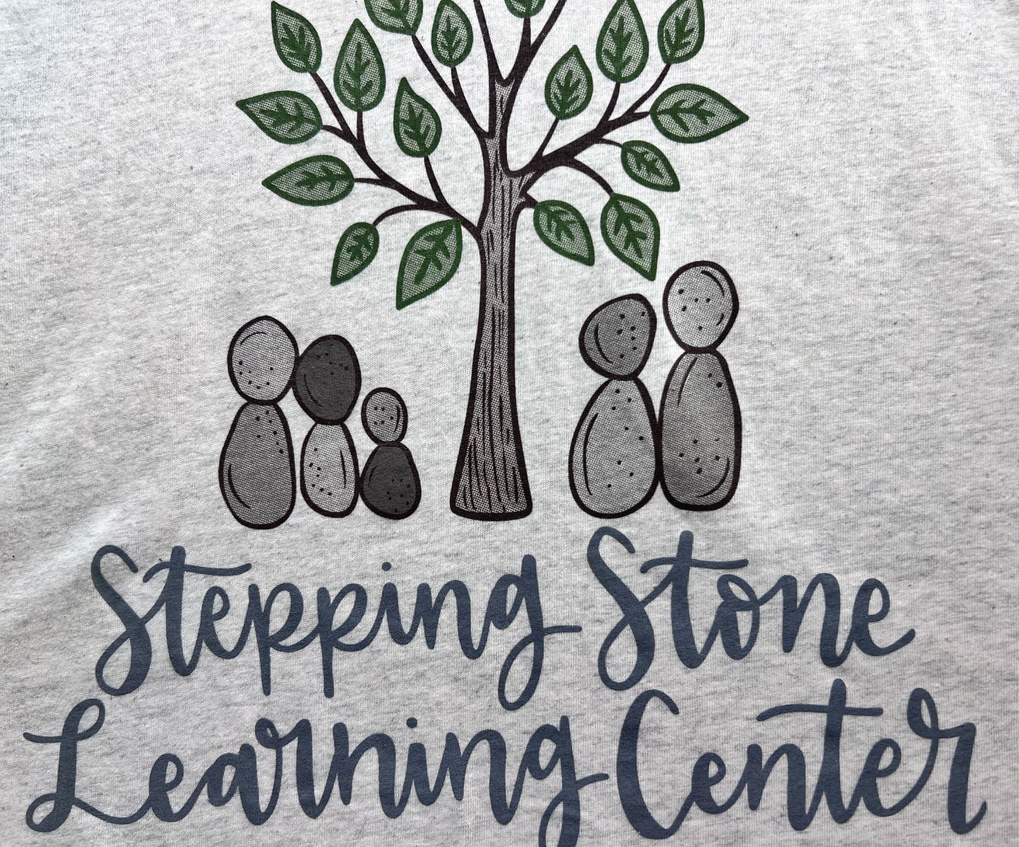 custom silk screened logo for Stepping Stone Learning Center: tree with stone figures under it; gray, green, and black.