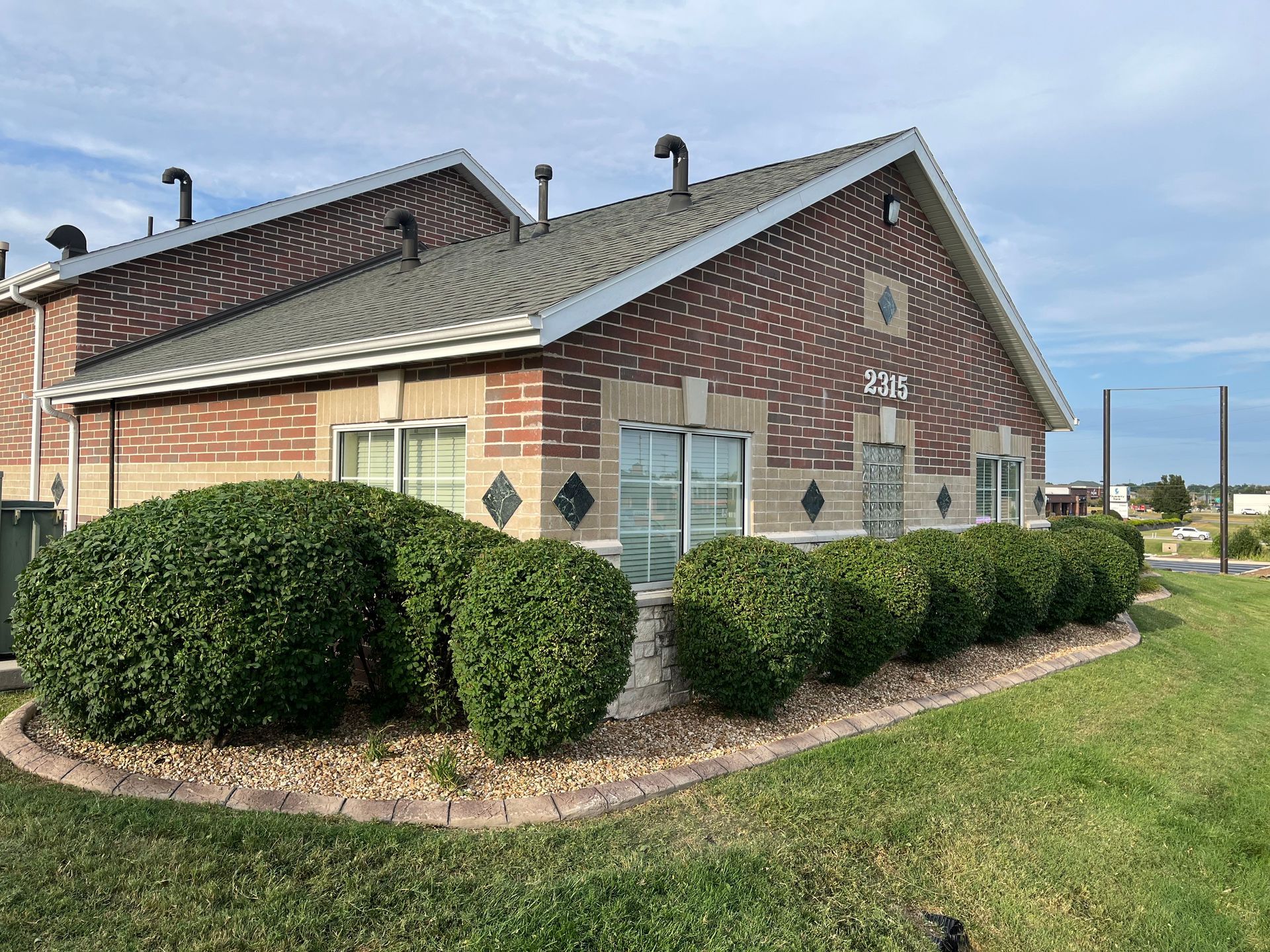 Single-story brick commercial building with a row of manicured shrubs along the front exterior.