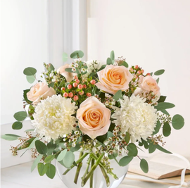 Peach and white floral bouquet in a glass vase on a bright table