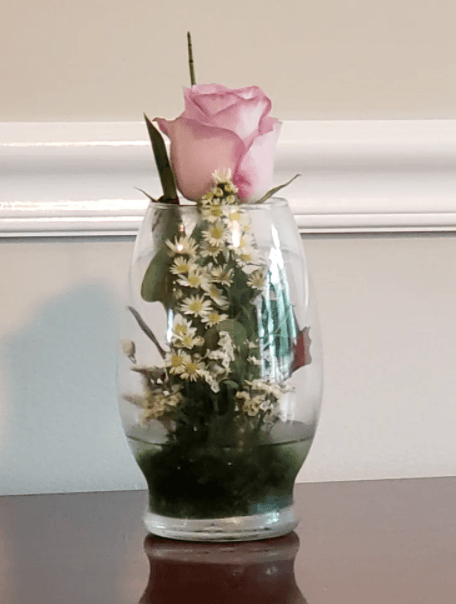 Pink rose and white flowers arranged in a clear glass vase on a table