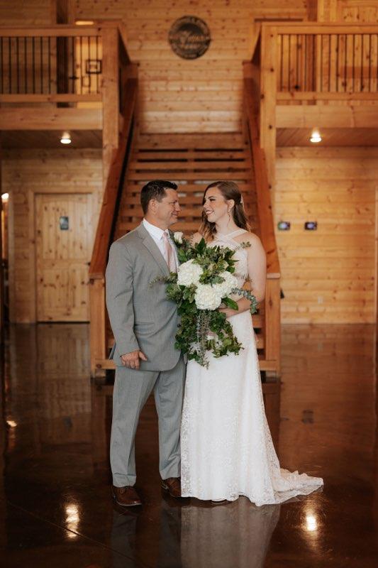 Bride and groom standing together in a wooden lodge, smiling and holding a bouquet.