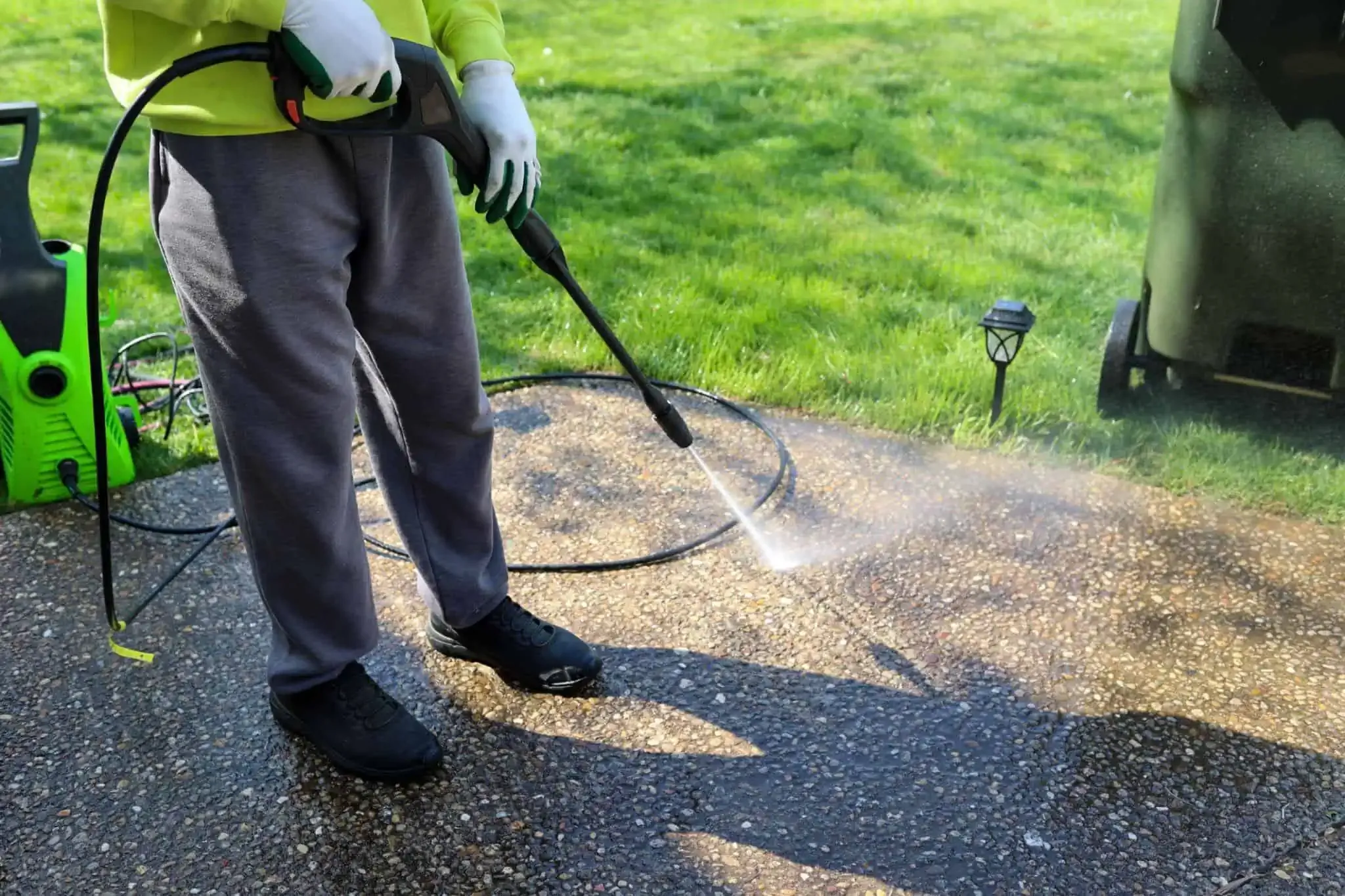 Lawn care worker mowing a green front yard with a push mower, facing a white house and driveway.