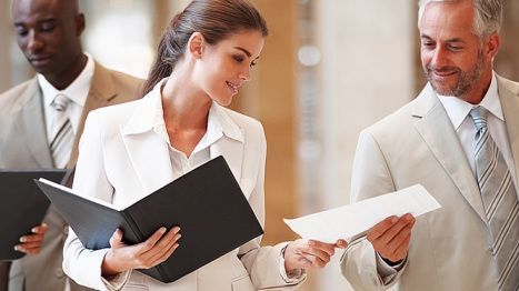 A group of business people are standing next to each other looking at papers.