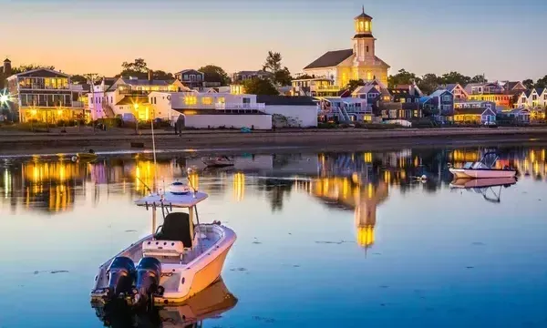 A boat is floating on top of a body of water with a Provincetown MA in the background.
