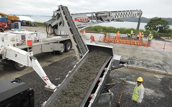 A man in a hard hat is standing next to a conveyor belt filled with concrete.