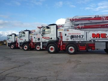 A row of concrete pump trucks are parked in a parking lot.