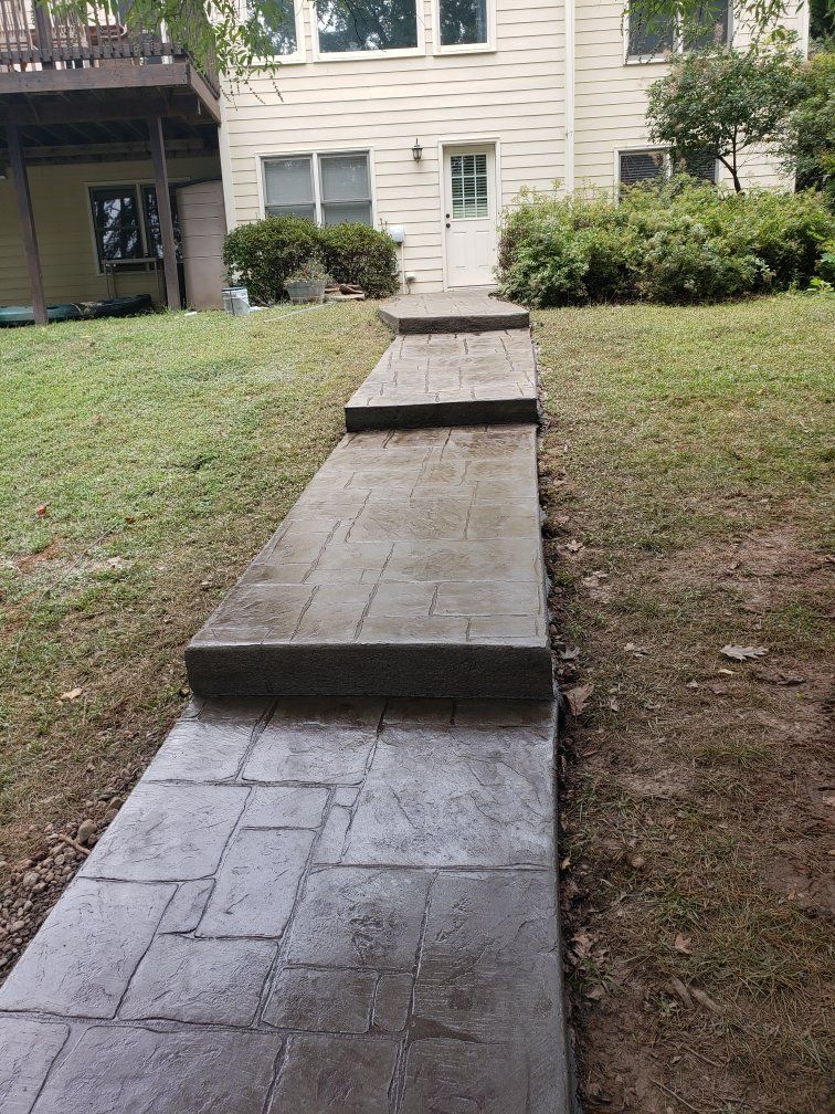 Concrete walkway with three raised steps leading to a beige apartment building across a grassy lawn